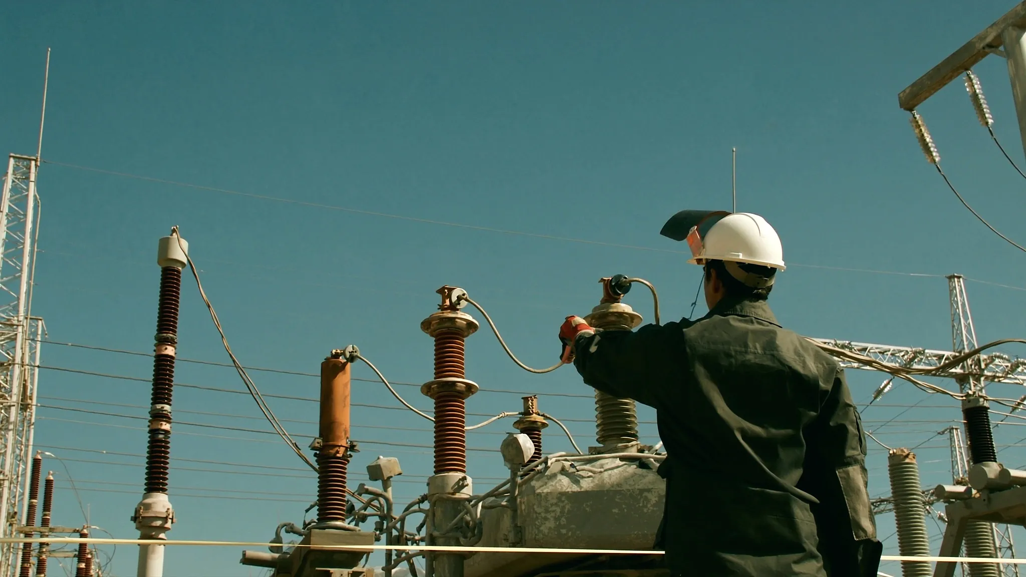 Técnico con equipo de protección contra arco eléctrico inspecciona con cámara termográfica una subestación desde la línea de barrera
