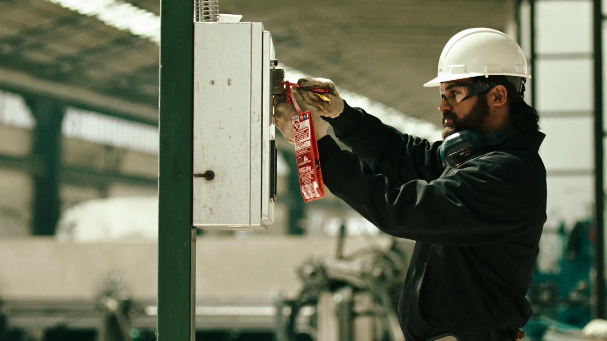 Técnico de mantenimiento instala candado y tarjeta de bloqueo en un tablero eléctrico de una planta industrial